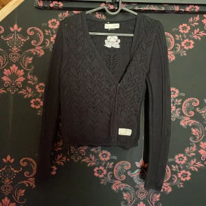 Svart stickad kofta från Odd Molly - Säljer en elegant svart stickad kofta från Odd Molly med v-ringning och ett vackert spetsmönster. Koftan har långa ärmar och en fin broderad detalj på baksidan. Perfekt för att lägga till en touch av stil till din garderob. knappt använd