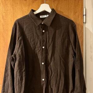Brun långärmad skjorta från Weekday - Säljer en stilren brun skjorta från Weekday med klassisk krage och vita knappar framtill. Skjortan är långärmad och har en rak passform, perfekt att styla till olika outfits. Skjortan stryks självklar innan frakt.