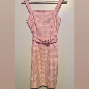 Rosa rutig klänning med bälte - Supersöt rosa och vit rutig klänning med breda axelband och tillhörande bälte i midjan. Klänningen har en rak passform och är knälång, perfekt för sommarens alla tillfällen. Snygg och feminin med klassiskt rutmönster.