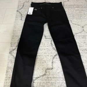 Svarta jeans från Lacoste - Snygga svarta jeans från Lacoste med klassisk femficksdesign och Lacoste-logga på fickan. Byxorna har raka ben och normal passform, perfekta för en stilren look. Materialet är slitstarkt och bekvämt.