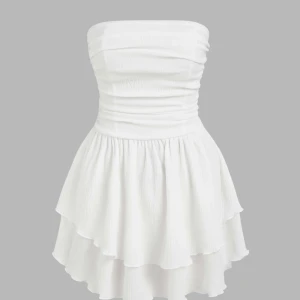 Vit axelbandslös klänning  - Säljer en söt vit axelbandslös klänning med omlottkjol och volangdetaljer. Klänningen har en tight passform upptill och en luftig kjol som ger en romantisk känsla. Perfekt för sommarens alla tillfällen!