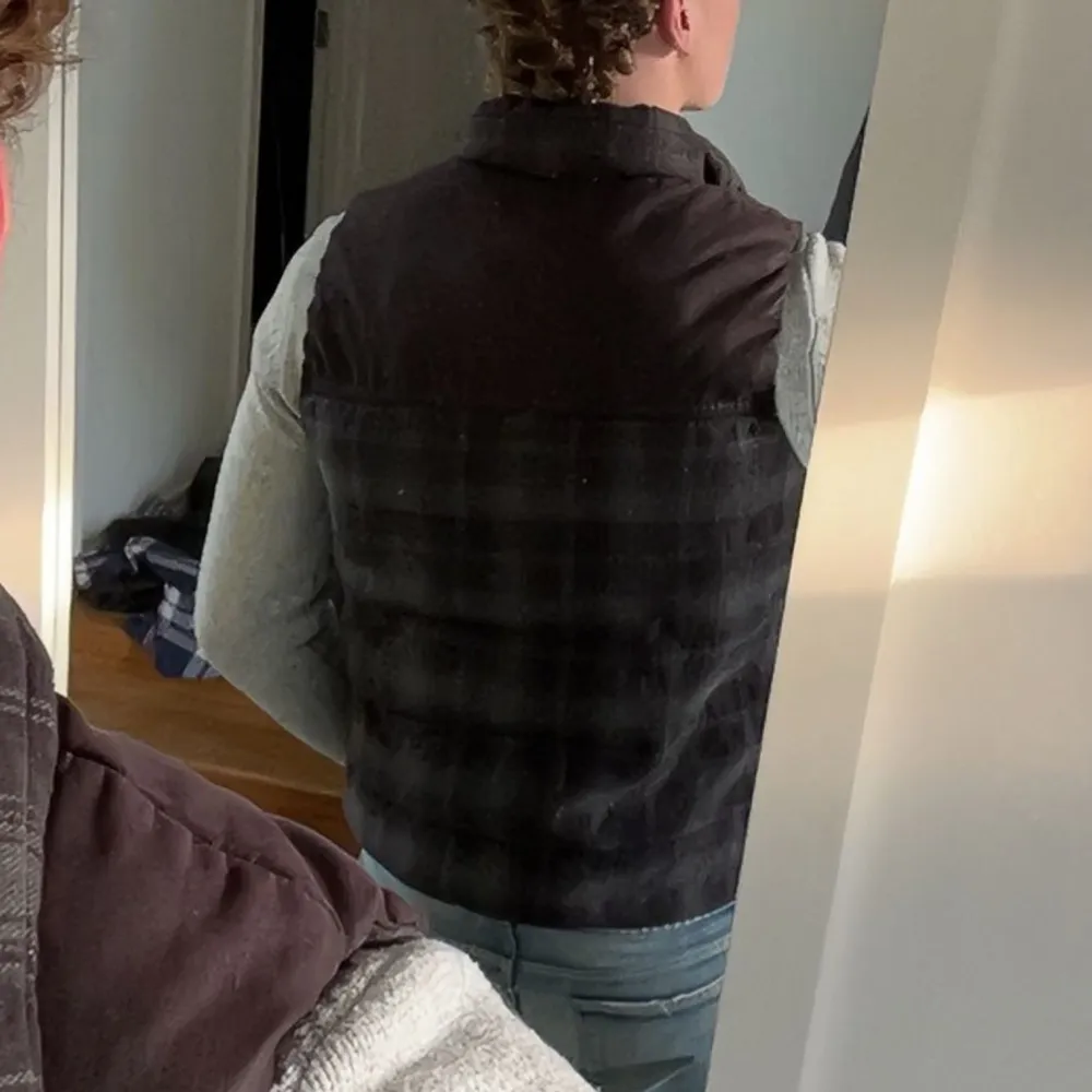 Säljer en gråbrun rutig väst med dragkedja framtill och två stora fickor. Västen har en hög krage och är vadderad för extra värme. Perfekt att bära över en tröja under kyliga dagar.. Takit.