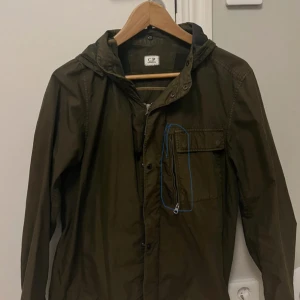 Cp company overshirt  - Säljer en olivgrön jacka från C.P. Company med huva och unika glasögondetaljer på baksidan. Jackan har dragkedja och knappar framtill samt en praktisk bröstficka med dragkedja. Perfekt för en stilren look. Storlek L men passar även M. OBS: den inringade fickan på första bilden går inte att stänga därav priser annars är jackan i suveränt skick!!
