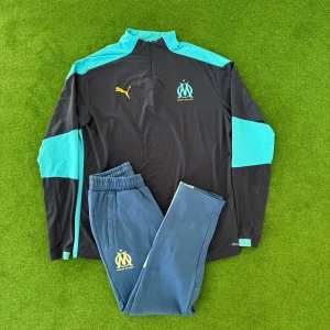 Marseille träningsbyxor från Puma - Säljer ett par blå träningsbyxor från Puma med Marseille-logga på benet. Byxorna har resår i midjan och är perfekta för fotboll eller träning. Matchande överdel finns också om du vill ha ett komplett set.