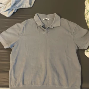 Ljusblå piké t-shirt från Zara  - Säljer en stilren ljusgrå piké t-shirt med klassisk krage och korta ärmar. Perfekt för en avslappnad men ändå snygg look. Passar till det mesta och är enkel att matcha med andra plagg.