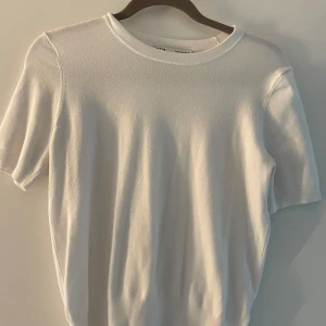 Vit kortärmad tröja från Zara - Säljer en stilren vit tröja från Zara. Den har korta ärmar och en rund halsringning, perfekt för en minimalistisk look. Tröjan är i en mjuk och bekväm kvalitet.