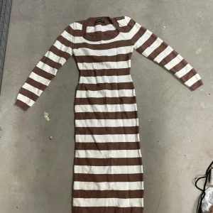 Brun- och vitrandig stickad långklänning från SHEIN - Stickad långklänning från SHEIN i brunt och vitt med breda horisontella ränder. Klänningen har lång ärm och rund halsringning. Perfekt för dig som gillar en enkel men snygg look.