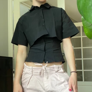 Svart croppad skjorta från Zara  - Säljer en svart skjorta med unik croppad design och korta ärm. En slutsåld skjorta från Zara. Jag säljer pågrund av att jag köpt två storlekar. På bilden bär jag storlek S men jag säljer storlek XS!! Super cool och trendig topp. Helt Oanvänd!🫧🫶🏼