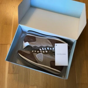 Bruna sneakers från Philippe Model - Snygga bruna sneakers från Philippe Model med vita och beige detaljer. Skorna har en rund tå och snörning framtill. Tillverkade i Italien med en stilren design som passar perfekt för en avslappnad look.