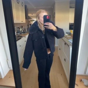 Svart teddyjacka med krage - Säljer en svart teddyjacka med stor fluffig krage och knappar framtill. Jackan är croppad och har en oversized passform med långa ärmar. Perfekt för dig som vill ha en mysig och trendig look.