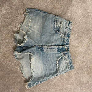 Blå jeansshorts från Zara - Säljer ett par snygga blå jeansshorts från Zara med fransiga kanter. Perfekta för sommardagar och ger en avslappnad look. De har en klassisk femficksdesign och är tillverkade i ett slitstarkt denimtyg.