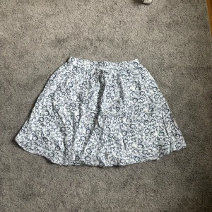 Blommig kjol från Ceamie - Säljer en söt blommig kjol från Ceamie i blått och vitt. Kjolen har en elastisk midja för extra komfort och är perfekt för varma dagar. Den har ett vackert blommönster som ger en fräsch och somrig känsla.