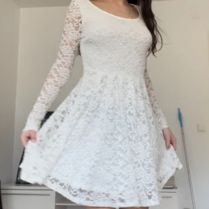 Studentklänning  - Charmig vit spetsklänning med långärmade ärmar och en rund halsringning. Klänningen har en vacker spetsdesign som ger en romantisk känsla. Perfekt för speciella tillfällen.