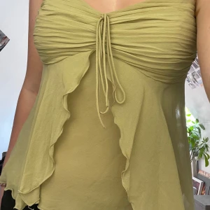 Ljusgrön volangtop - Supersöt ljusgrön topp med volangdetaljer och knyt framtill. Toppen har tunna axelband och rynkade partier över bysten. Perfekt för varma dagar och ger en romantisk vibe. Tyvärr har tröjan fått en liten fläck på baksidan, se sista bilden.