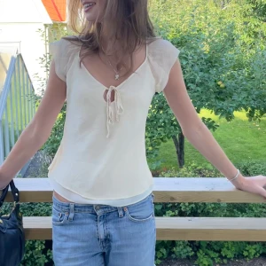 Gul blus från GAP - Säljer en söt gul blus från GAP med v-ringning och knyt framtill. Blusen är ärmlös och har en lätt, luftig känsla som passar perfekt till varma dagar. Enkel att matcha med jeans eller kjol för en avslappnad look.