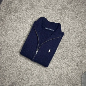 Ralph Lauren Kabelstickad Hel-Zip - Ralph Lauren Kabelstickad Hel-Zip – Mörkblå (S) 🧵💙  Säljer en klassisk kabelstickad helzip-tröja från Ralph Lauren i en tidlös mörkblå färg. Tillverkad i mjukt och bekvämt material med dragkedja hela vägen och den ikoniska broderade loggan. Perfekt till vardag, skola eller jobb!  ✅ Storlek: S 📏 Mått: Längd 60 cm, armhåla till armhåla 50 cm, axel till axel 45 cm 🎨 Färg: Mörkblå 👕 Modell: Kabelstickad Hel-Zip 🏷 Märke: Ralph Lauren 💸 Nypris: ca 2800 kr – säljs till ett kap!  📍 Finns för avhämtning 