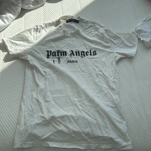 Vit t-shirt från Palm Angels - Säljer en vit t-shirt från Palm Angels med svart text på framsidan. T-shirten har en klassisk passform och är kortärmad. Perfekt för en avslappnad stil.