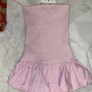 Rosa klänning med volangdetalj - Säljer denna söta rosa bandeau klänning med volang!💗💗 Klänningen är i storlek S, men passar även XS och i nytt skick! Passformen är tight mot kroppen men stretchig och den har även en dragkedja på sidan!💗💗