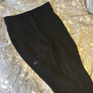Svarta ridbyxor från Fager - Snygga svarta ridbyxor från Fager med hög midja och halvskoning. Byxorna har en knapp och dragkedja framtill samt praktiska fickor för mobilen på båda benen. Endast använda ett fåtal gånger. Storlek 38 och modell Freya Hybrid. Nypris: 1299kr