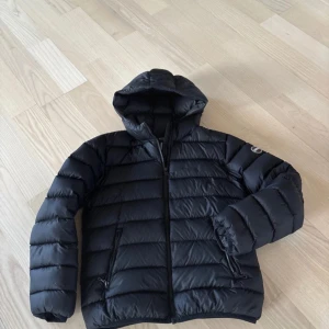 Svart dunjacka från Colmar - Snygg svart dunjacka från Colmar med huva och dragkedja. Använd en säsong och finns ett litet hål vid armen, kan skickas bild på. Nypris är 4500kr