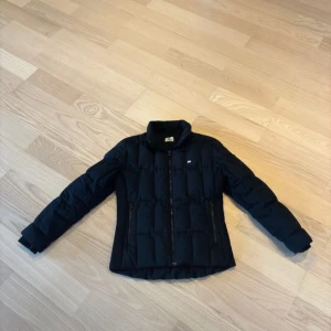 Svart dunjacka från Lacoste - Säljer en stilren svart dunjacka från Lacoste med dragkedja framtill. Sälja då den inte kommit till supermycket användning 