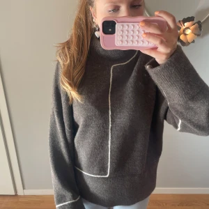Brun stickad tröja med vit detalj - Säljer en brun stickad tröja med en unik vit linjedetalj. Tröjan har en hög krage och långa ärmar. Aldrig använd!! 