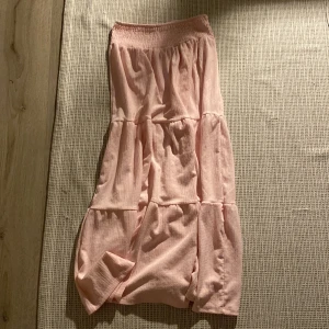 Ljusrosa volangkjol - Säljer en ljusrosa kjol med flera volanger och resår i midjan. Kjolen är lång och har en mjuk, lätt struktur i tyget som ger ett flowy intryck. Perfekt för dig som gillar en feminin och avslappnad stil.