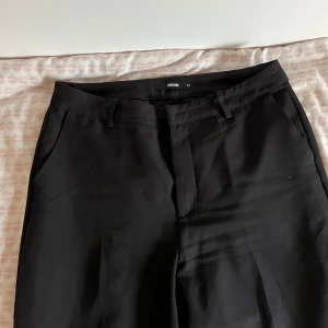 Svarta kostymbyxor från BikBok - Säljer ett par klassiska svarta kostymbyxor från BikBok. Byxorna har normal passform, raka ben och hällor för bälte. Perfekta till en stilren look och passar till många olika tillfällen.