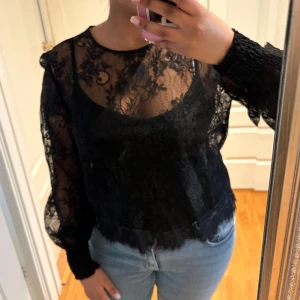 Svart spetsblus med lång ärm - Säljer en svart blus i spets med transparenta partier och lång ärm. Blusen har rund halsringning och fina spetsdetaljer över hela plagget. Perfekt för dig som vill ha en elegant och trendig look.