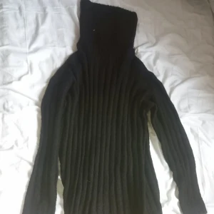 Svart ribbad stickad klänning - Säljer en svart stickad lång klänning med ribbad struktur och långa ärmar. Klänningen har en åtsittande passform och har en polokrage, perfekt för kyliga dagar. Enkel och stilren design som passar till det mesta.