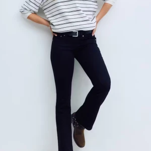 Svarta low waist bootcut jeans Y2K - Svarta bootcut jeans med låg midja i klassisk Y2K-stil. Jeansen har fem fickor, silverfärgade knappar och dragkedja. Snygg passform med utsvängda ben och tightare upptill. Perfekta till sneakers eller boots för en cool vardagslook.