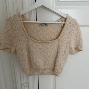 Beige stickad crop topp från Chiquelle - Superfin croppad topp i beige från Chiquelle med korta ärmar och snyggt stickat mönster. Toppen har en fyrkantig ringning och ribbade kanter som ger en trendig vibe. Perfekt att styla med höga jeans eller kjol för en chill look.