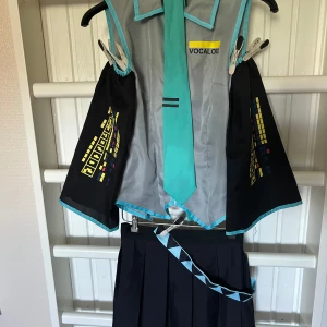 Hatsune Miku Vocaloid cosplay kostym med slips - Säljer en Hatsune Miku vocaloid Cosplay. Hennes blus, ärmar, kjol, bälte och slips ingår. Inga strumpor och ingen peruk.