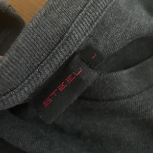 Mörkgrå långärmad tröja från Steel - En basic mörkgrå långärmad tröja från Steel i storlek L. Tröjan har en enkel rund halsringning och är tillverkad i mjukt material, perfekt för lager-på-lager eller chill dagar. Passar dig som gillar stilren och clean look.