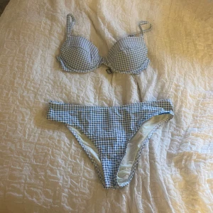 Blåvit rutig bikini med bygel - Supersöt bikini med blåvitt rutigt mönster från P.C. Ullared. Överdelen har bygel och justerbara axelband, medan underdelen är högt skuren. Perfekt för strandhäng och poolparty! Materialet känns mjukt och följsamt mot huden. Lite missfärgad av solkräm, där av priset.
