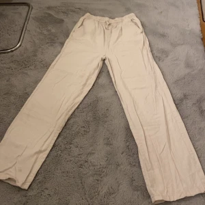 Beiga linnebyxor med resårmidja - Snygga och luftiga beiga linnebyxor med resår i midjan och raka ben. Perfekta för varma dagar!  Byxorna har en avslappnad passform och är tillverkade i mjukt linnematerial som andas. Stolek 158/164. Har en liten fläck på vänster ben, men inget som stör användning! Köpta från Ullared för nått år sen, men inte använda mer än 5 -6 gånger. Passar både tjejer och killar! Kontakta mig om ni vill ha fler bilder eller om ni är intresserade. (Kan självklart stryka byxorna om det önskas)