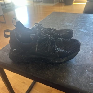 Svarta sneakers från Puma - Svarta sneakers från Puma med stickad ovandel och snyggt vävt mönster. Skorna har rund tå, platt sula och snörning för en sportig look. Perfekta för dig som gillar stilrena och bekväma skor till vardags och till löpning. 