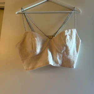 Beige linnetopp med glittriga axelband - Superfin beige linnetopp med glittriga silverfärgade axelband. Toppen är croppad och har en snygg formad byst. Perfekt för dig som vill ha en enkel men ändå extra look. Materialet är linne och toppen har en stilren, minimalistisk vibe.