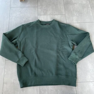 Mörkgrön sweatshirt från Pull&Bear - Enkel och stilren mörkgrön sweatshirt från Pull&Bear i mjuk bomull. Tröjan har rund halsringning, långa ärmar och ribbade muddar vid ärmslut och nederkant. Perfekt för en chill och avslappnad look.