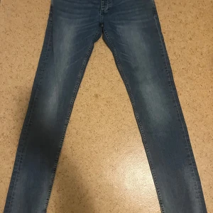 Blå slim jeans Jack & Jones 30/34 - Snygga blå skinny jeans från Jack & Jones i klassisk tvätt. Jeansen har normal midja, fem fickor och diskreta slitningar för en cool look. Perfekta till sneakers eller boots och passar dig som gillar en smal passform.