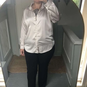 Ljus silkeslen skjorta med krage - Snygg ljus oversize skjorta i silkesliknande material med klassisk krage och långa ärmar. Skjortan har en avslappnad passform och knappar framtill. Perfekt för dig som gillar stilrena och eleganta plagg. Passar M-L 