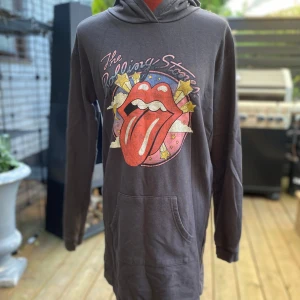 Rolling Stones hoodie från H&M 170 - Svart hoodie från H&M med Rolling Stones-tryck framtill. Tröjan har huva, lång ärm och en stor magficka. Materialet är mjukt och skönt, perfekt för dig som gillar bandmerch och streetstyle. Snyggt tryck med tungan och stjärnor i rött, gult och blått.