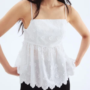 Vit broderad topp - Superfin vit linnetopp med tunna axelband och broderade blommor över hela tyget. Toppen har volangkant nertill, öppen rygg med knyt och en luftig, flowy passform. PRIS KAN DISKUTERAS!