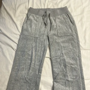 Grå mjukisbyxor Juicy Couture XS - Supermysiga grå mjukisbyxor från Juicy Couture med bred resår och snörning i midjan. Byxorna har stora fickor fram och bakfickor med lock och knappar. Perfekta för chill dagar eller när du vill vara extra comfy.