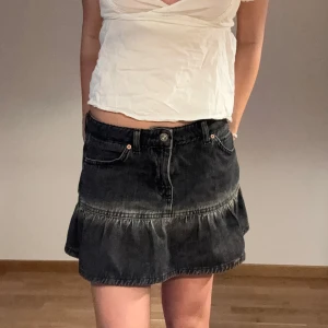 Lågmidjad jeanskjol med volang - Snygg svart jeanskjol med volangkant och klassiska fickor fram. Midjemått: 38cm, Längd: 32cm, Storlek: S
