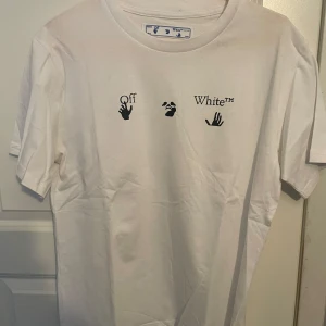 Vit Off-White t-shirt med blå print - Vit t-shirt från Off-White med svart tryck framtill och stor blå grafisk print på ryggen. Klassisk passform med rund hals och korta ärmar. Materialet är mjuk bomull och designen har en modern streetwear vibe.