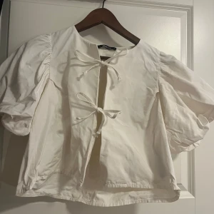 Vit blus med puffärm från Gina Tricot - Supersöt vit blus från Gina Tricot med puffiga korta ärmar och två knytningar framtill. Blusen har en rak passform.