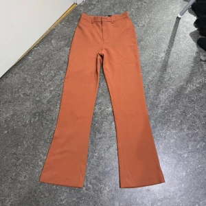 Rostfärgade bootcut-byxor BikBok XS - Snygga rostfärgade byxor från BikBok i bootcut-modell. Byxorna har hög midja, bälteshällor och stängs med dragkedja och knapp. Materialet känns mjukt och har en lätt stretch, perfekt för en trendig look.