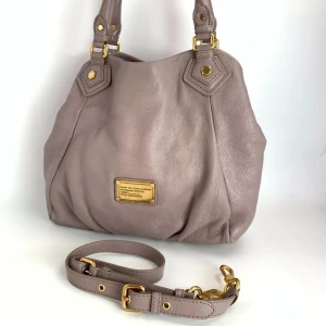 Beige skinnväska Marc by Marc Jacobs - Snygg beige handväska från Marc by Marc Jacobs i mjukt skinn med guldfärgade metalldetaljer. Perfekt för skolan, dator och annat får plats. Säljer då jag har en likadan i svart jag använder mer🩷