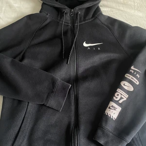 Nike Air hoodie  - Säljer denna snygga svarta Nike-hoodie med dragkedja – perfekt för dig som älskar streetwear med en clean look! Modellen är stilren framtill med det klassiska Nike Air-loggan på bröstet och en galet snygg detaljärm med flera ikoniska Air Max-symboler, inklusive “97”, “air max” och japansk text – en hoodie du inte ser varje dag!  ✔️ Original Nike ✔️ Mjuk & varm insida ✔️ Perfekt passform ✔️ Snygga tryck – både fram och på ärmen ✔️ praktiska fickor  ✅ I mycket fint skick – knappt an